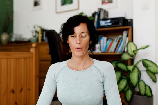Adult female sitting with a straight back, eyes closed, and exhaling after looking at how to increase lung capacity