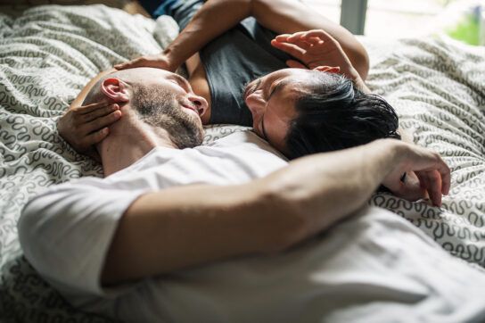 Couple lying together on bed with arms wrapped around each other's head