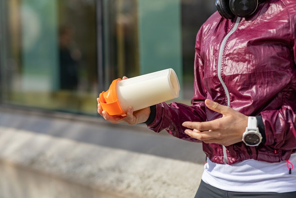 A person shown from the neck down standing outside, holding a protein shake, which can help you gain weight with diabetes.