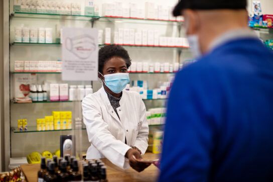 A pharmacist accepting a prescription discount card or drug coupon from a customer, perhaps explaining how they're different.