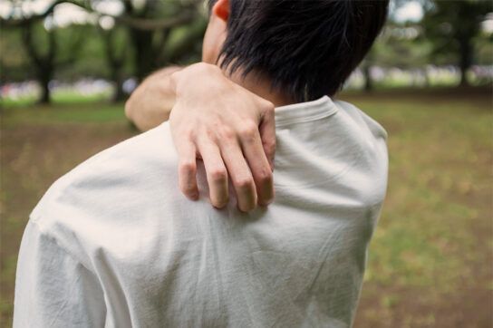 A young adult shown from behind scratching their back, a symptom of shingles in young adults.