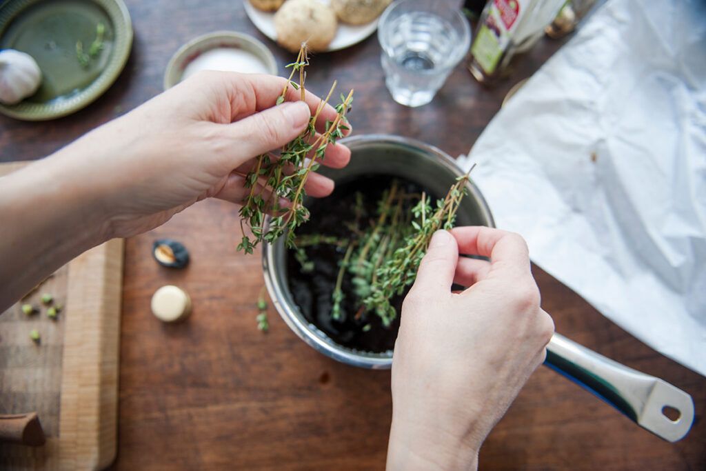 Woman putting dry herbs in a pot to prepare natural treatment for SIBO