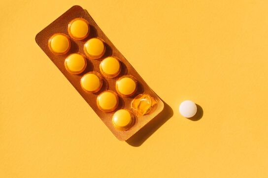 Top view of sealed and open blister packs with tablets placed near empty space on yellow background. Blister packs with round pills