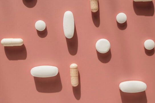 Various Capsules and Tablets on a Pink Background