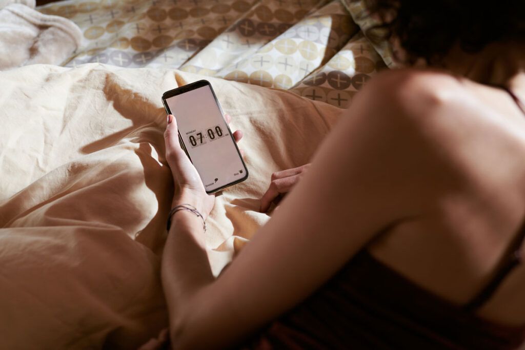 Person sitting up in bed and setting their morning alarm on their phone.