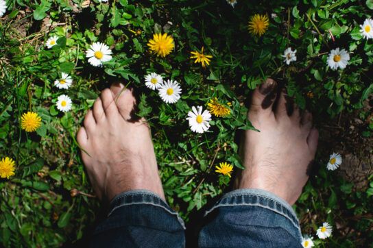 Person standing with bare feet on grass, surrounded by daisies.