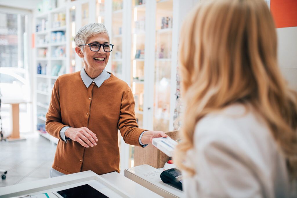 An older person smiling and taking a prescription from a pharmacist. They have recently found out how prescription discount cards work.