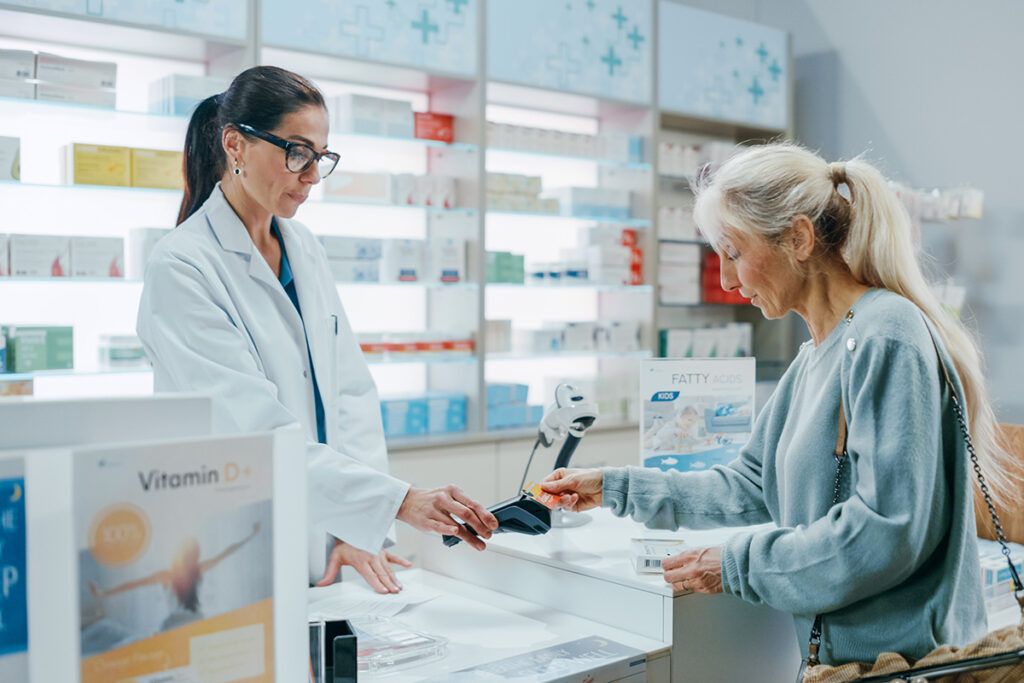 Adult female pharmacist passing a payment machine to an adult female in a pharmacy after they compare prescription discount cards