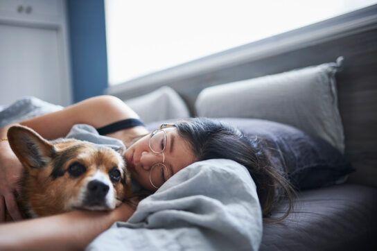 Young woman feeling sleepy from pednisone use while lying down with her dog