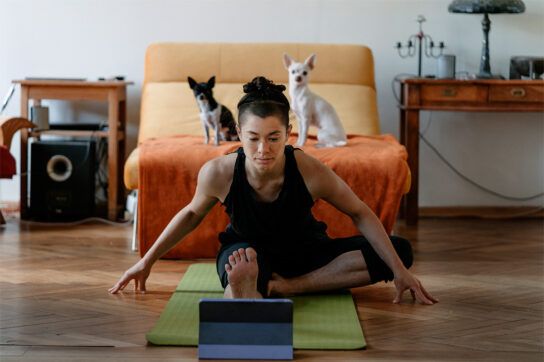 adult female sitting in a living room on a yoga mat practiwsing yoga poses iwth two small dogs behind her watching her. This may be after asking to question do statins cause weight gain