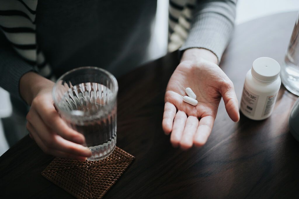 Overhead view of person's hand holding two white tablets with glass of water in other hand