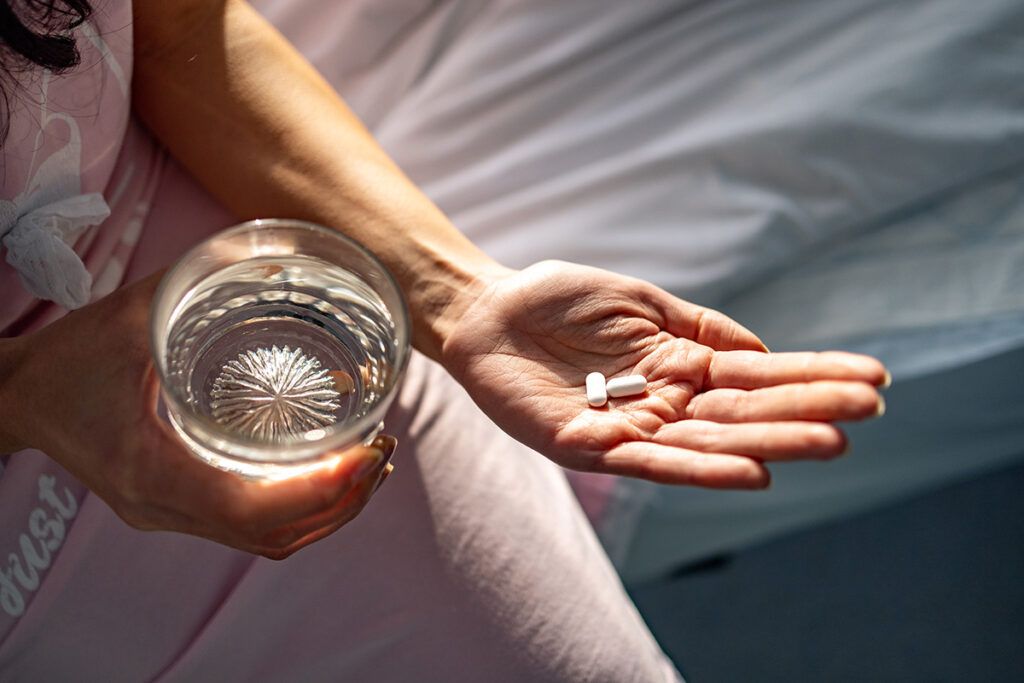 Person holding 2 pills in 1 hand a glass of water in the other to depict how long Zoloft takes to work.