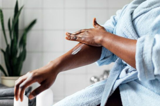 A person wearing a bathrobe applying cream to their arm. They may have a condition that can be mistaken for scabies.
