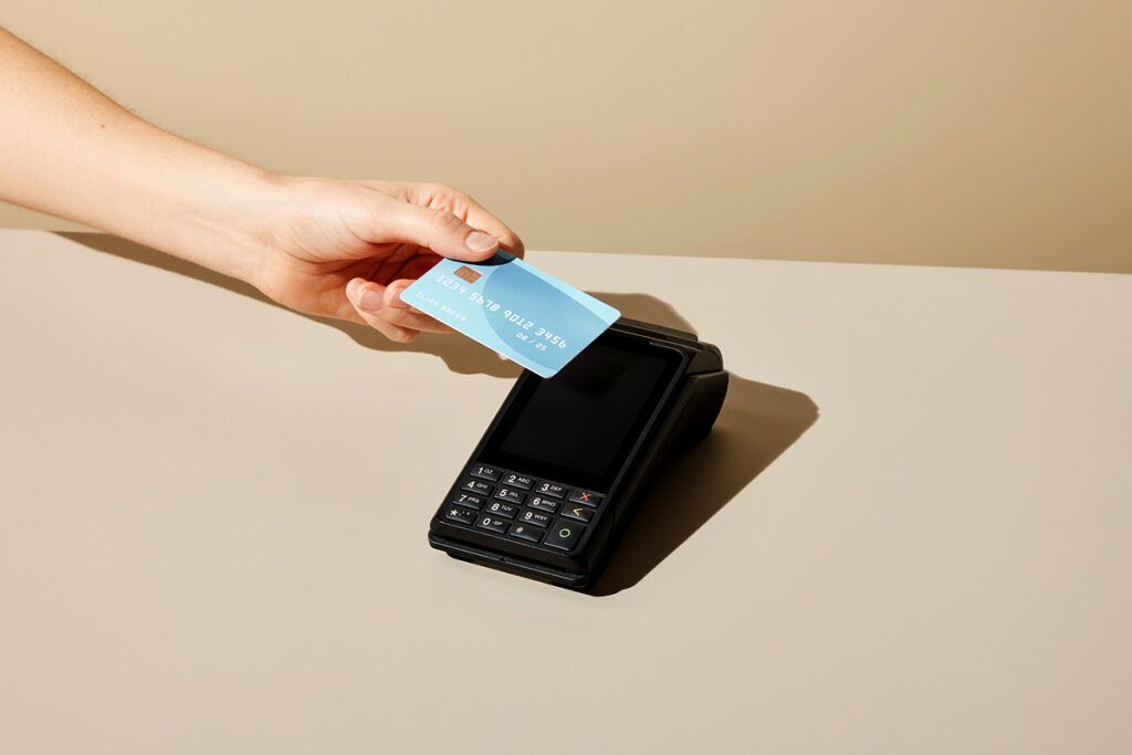 Someone's left hand and forearm reaching to tap an FSA card against a contactless credit card machine