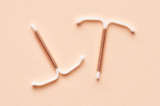 Two IUDs side by side on a pale peach background. IUDs may stop periods.