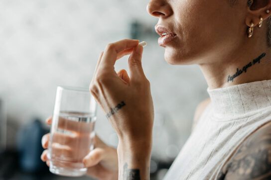 Person holding a glass of water in 1 hand and a Zoloft pill in the other.