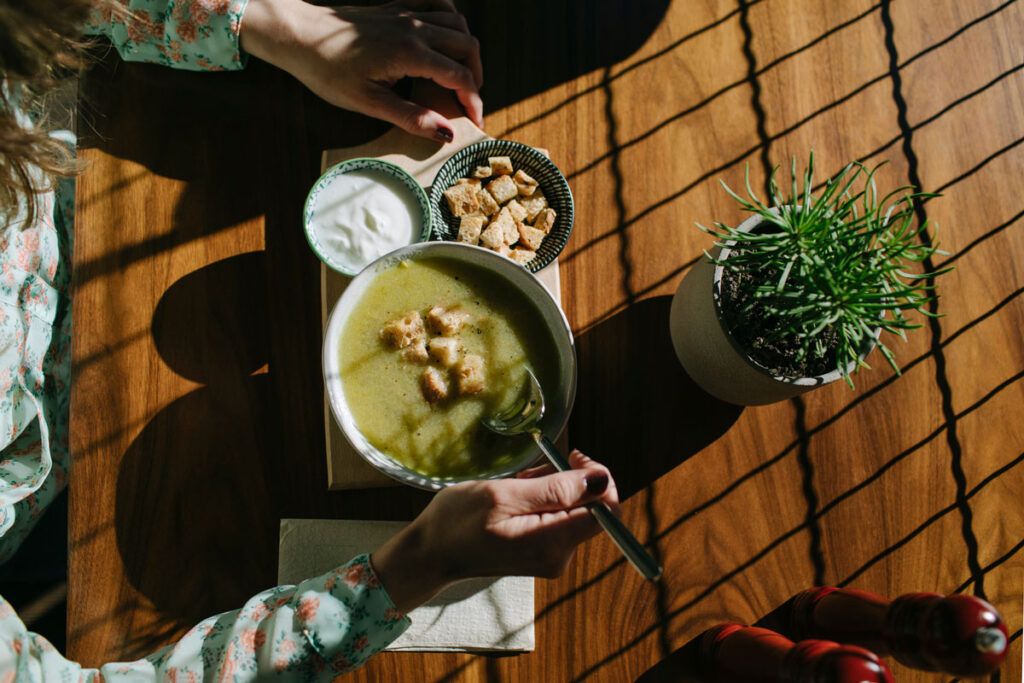 A person sitting at a table eating a green soup, which can form part of a vestibular migraine diet.