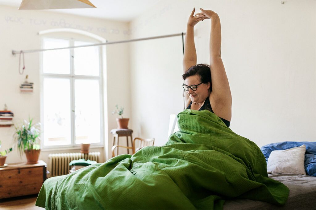 A person sitting up and stretching in bed. They may use muscle relaxers and wonder how they work.