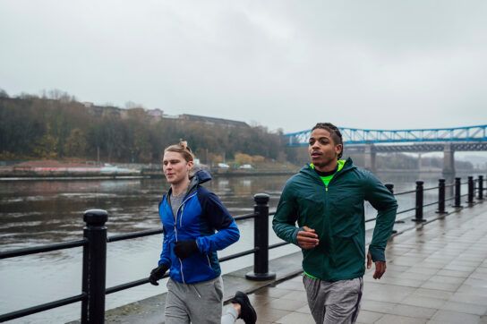 Two people going on a run next to a river to depict decreasing cortisol levels.
