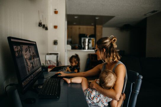 Female sitting at a computer desk with a young child in her arms to depict breastfeeding while on Zoloft.