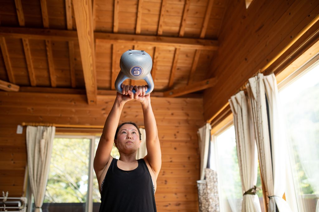A person lifting a heavy kettle bell weight, thinking of ways to prevent rhabdomyolysis, induced by exercise and weightlifting.