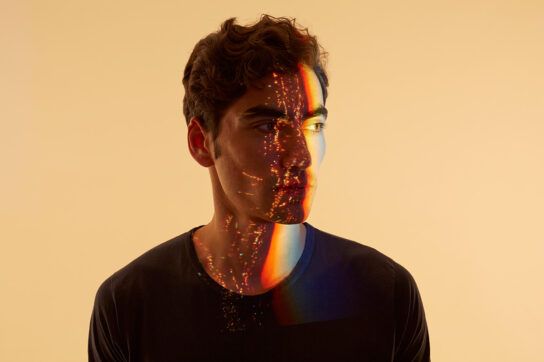 Man staring to his left while a rainbow and specks of light are reflected on to his face, to depict differences and similarities between serotonin and dopamine.