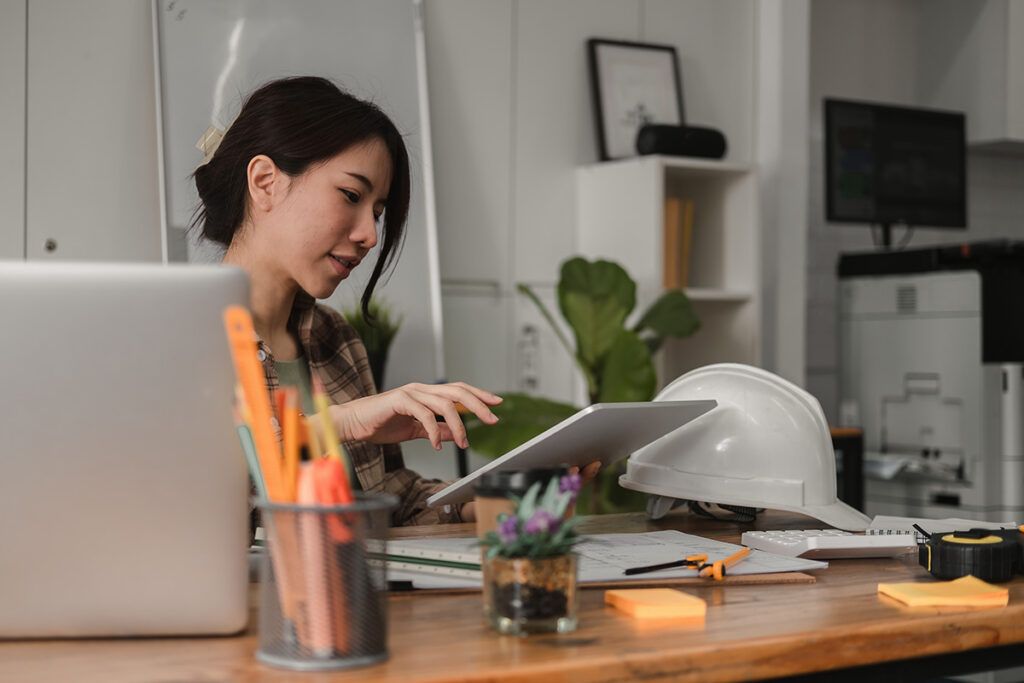 Adult female sitting at their at-home desk looking at tablet device for information on fsa vs. hsa