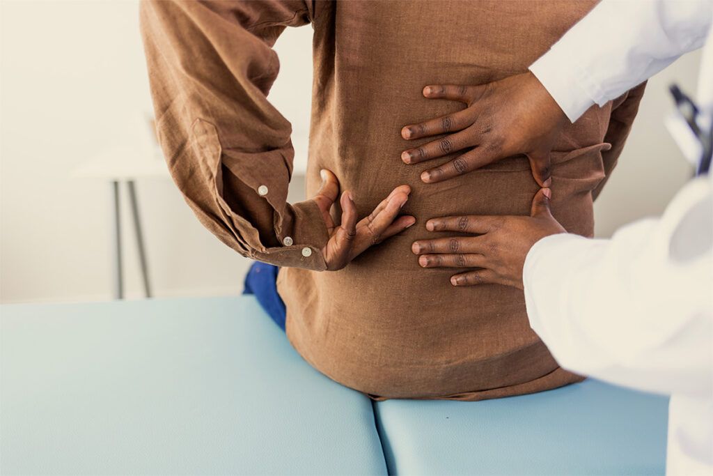 A doctor placing their hands on someone's lower back to check for kidney disease.