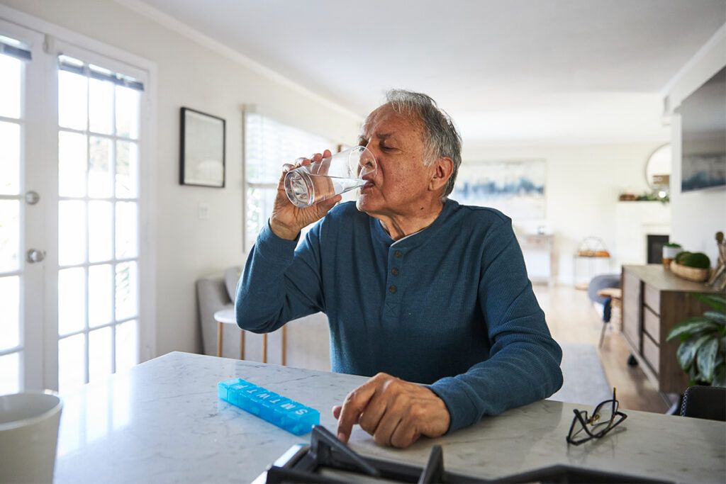 An older adult taking medication with a drink of water, considering how often you can take Zofran.