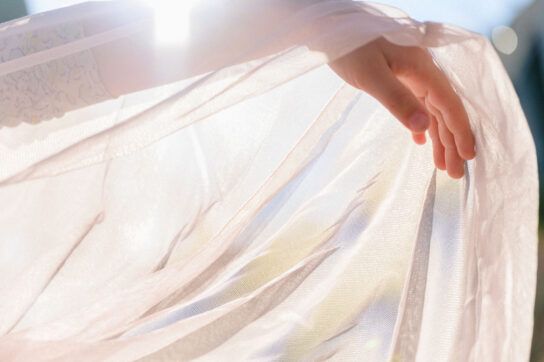 A person's arm holding up a very thin sheet with light shining through, representing medications causing thin skin.