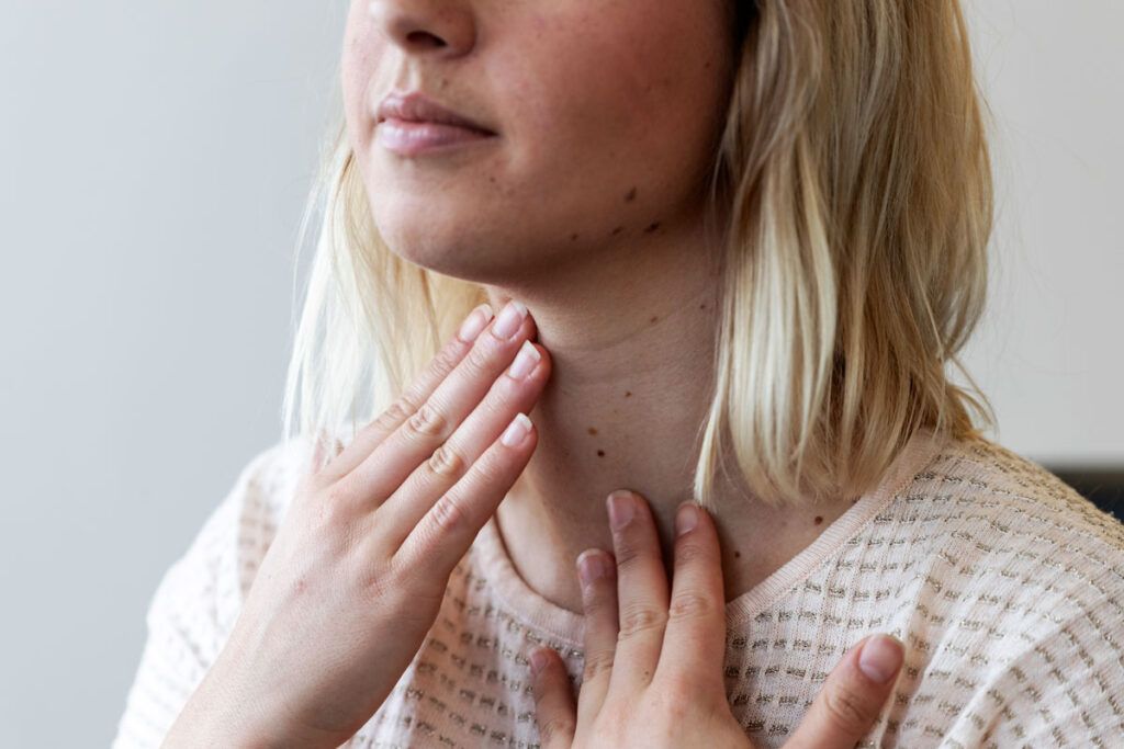 Female touching her throat to check her thyroid glands to depict the hypothyroidism medication levothyroxine.