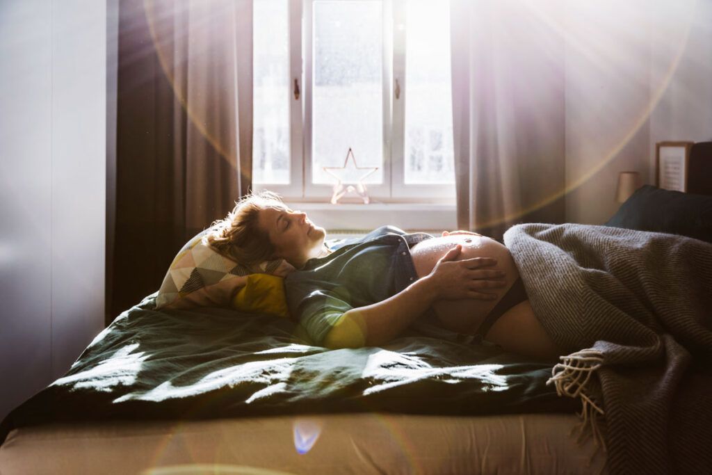 Pregnant woman laying down with her hands on her stomach to depict second-trimester fatigue.