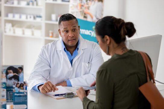 A person speaking with a healthcare professional at a pharmacy counter to depict what you need to know about the medication fenofibrate.