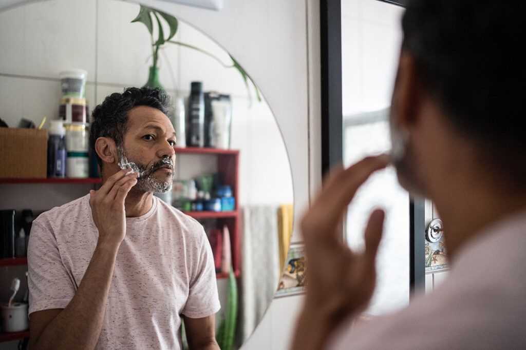 Adult male looking into a mirror and applying shaving cream, possibly wondering if there is any medication for ingrown hairs