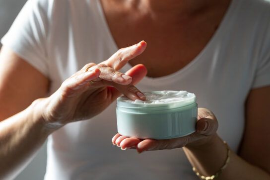 A person shown from the shoulders down dipping their fingers into tretinoin cream, which is a retinoid.