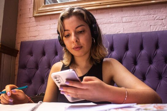 A young person studying and looking at their phone with headphones on, possibly researching Ritalin and Adderall for weight loss.