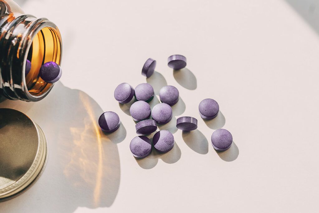 Overturned bottle and spilling out we see some purple pills for acid reflux