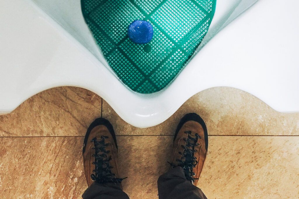 First person view of a person looking down at their shoes and a urinal as they wonder why some men have trouble urinating