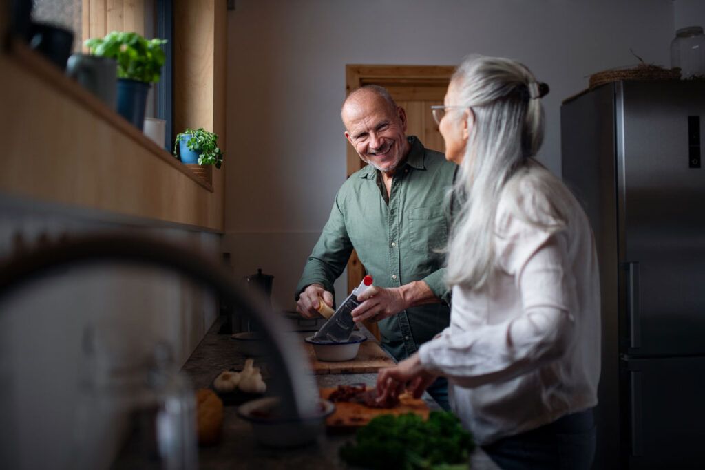 Two older adults enjoying a conversation and preparing food in a kitchen after looking up Ozempic foods to avoid