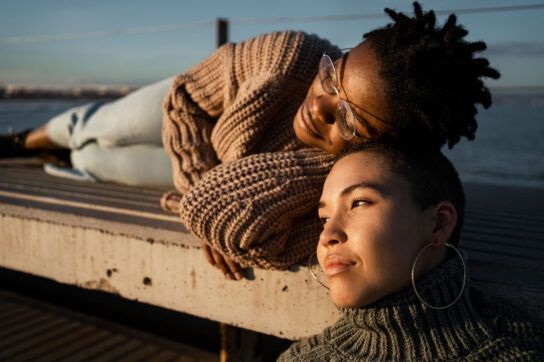 Two females sitting casually on bed looking toward sunset
