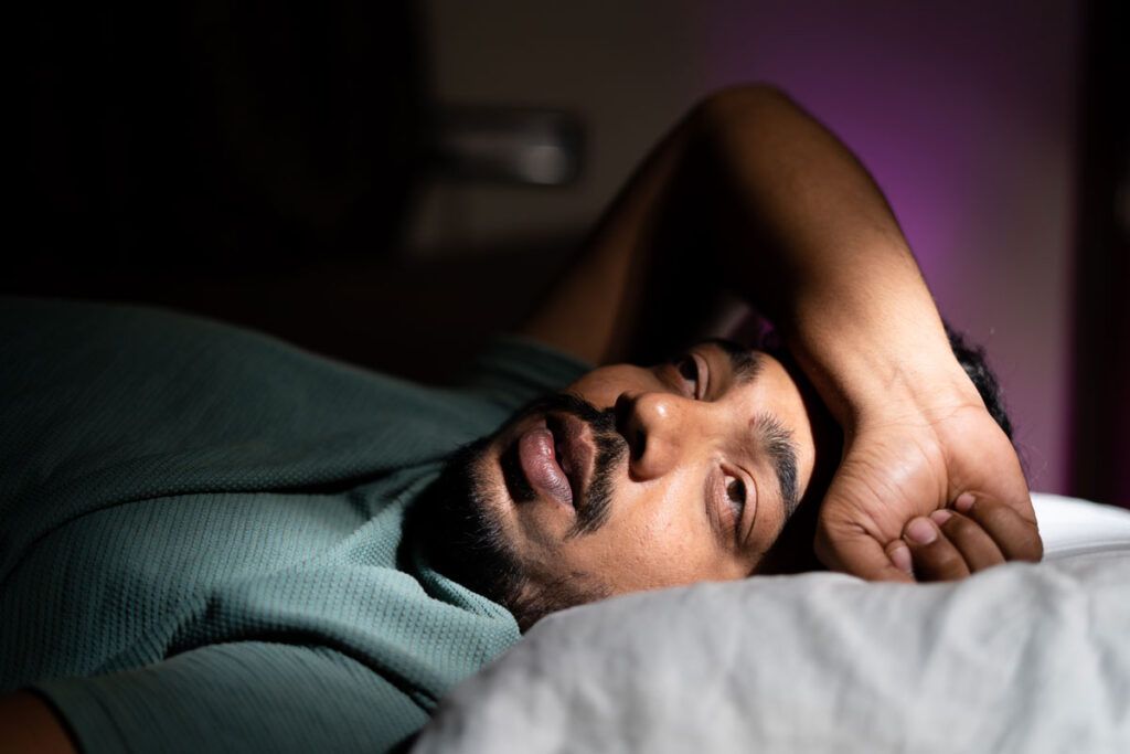 Man laying awake in bed to depict the question 'how much melatonin should I take?'