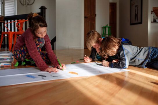 Three children drawing on a large piece of paper on the floor. They may take Adderall which can have different effects on the body.