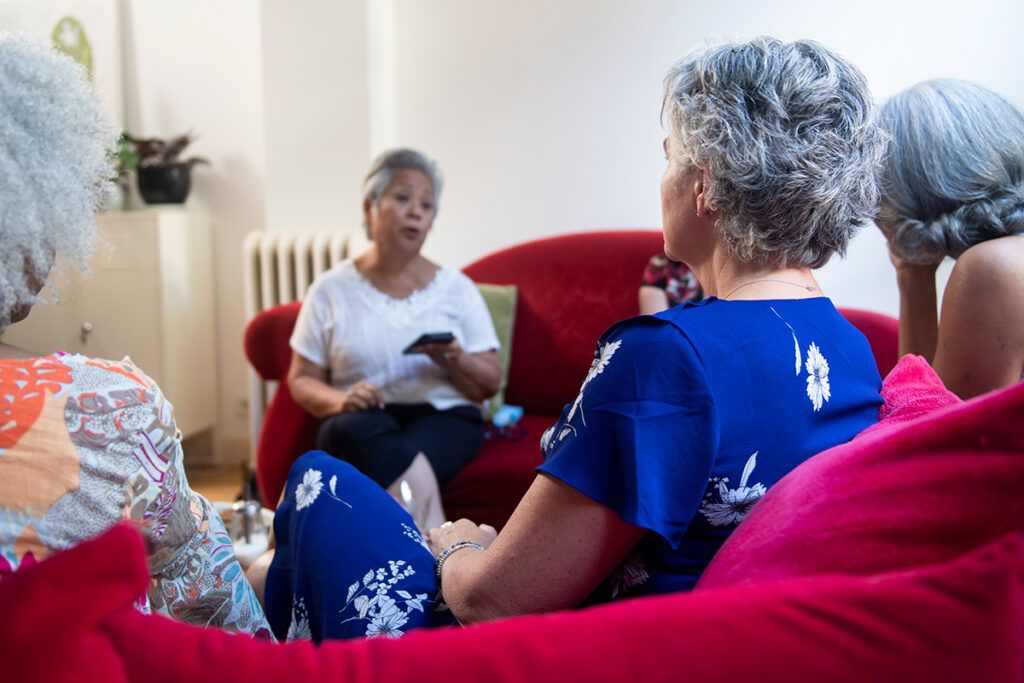 A group of older women sitting on sofas and chatting about ovarian cancer vs. cervical cancer.