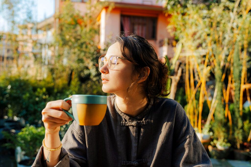 Female sat in the sun holding a mug, to depict how much sun you need a day.