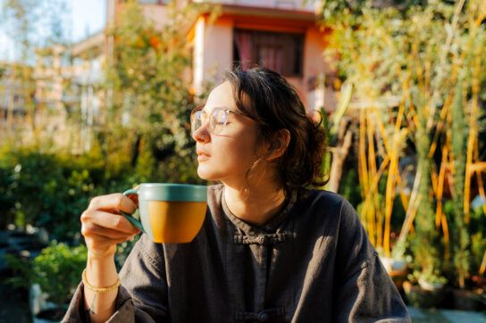 Female sat in the sun holding a mug, to depict how much sun you need a day.