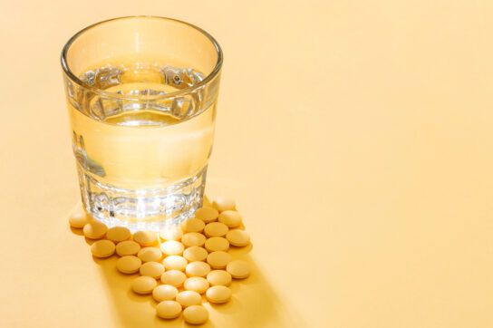 Yellow water pills next to a glass of water on a yellow background.