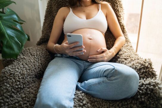 Pregnant woman's bare belly while she looks at her phone; metformin during pregnancy
