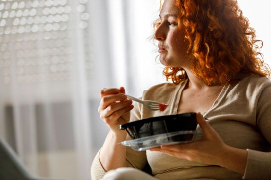 An adult sitting down eating a meal out of a tub, contemplating taking Tylenol on an empty stomach.