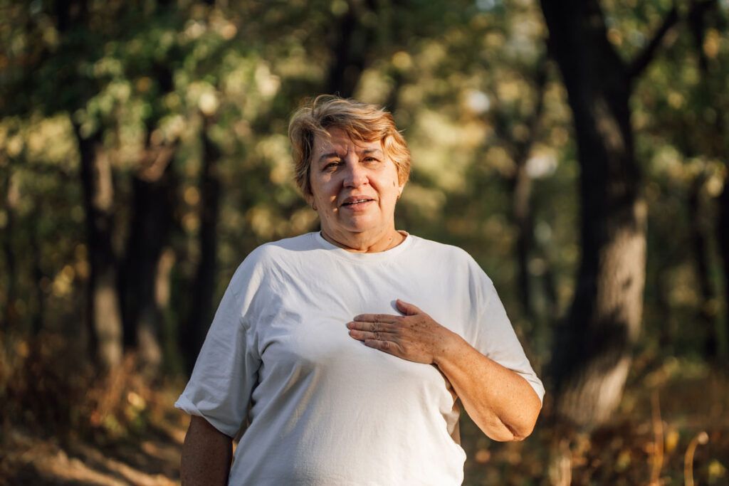 An older adult with their hand on their chest outdoors. They have symptoms of early COPD.