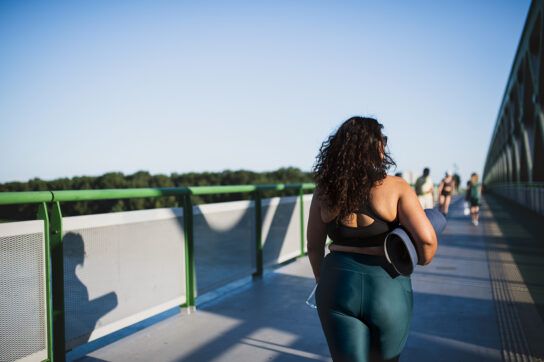 Adult female in workout clothing and a yoga mat under her arm walking across a bridge on a beautiful morning possibly contemplating does pioglitazone cause weight gain?
